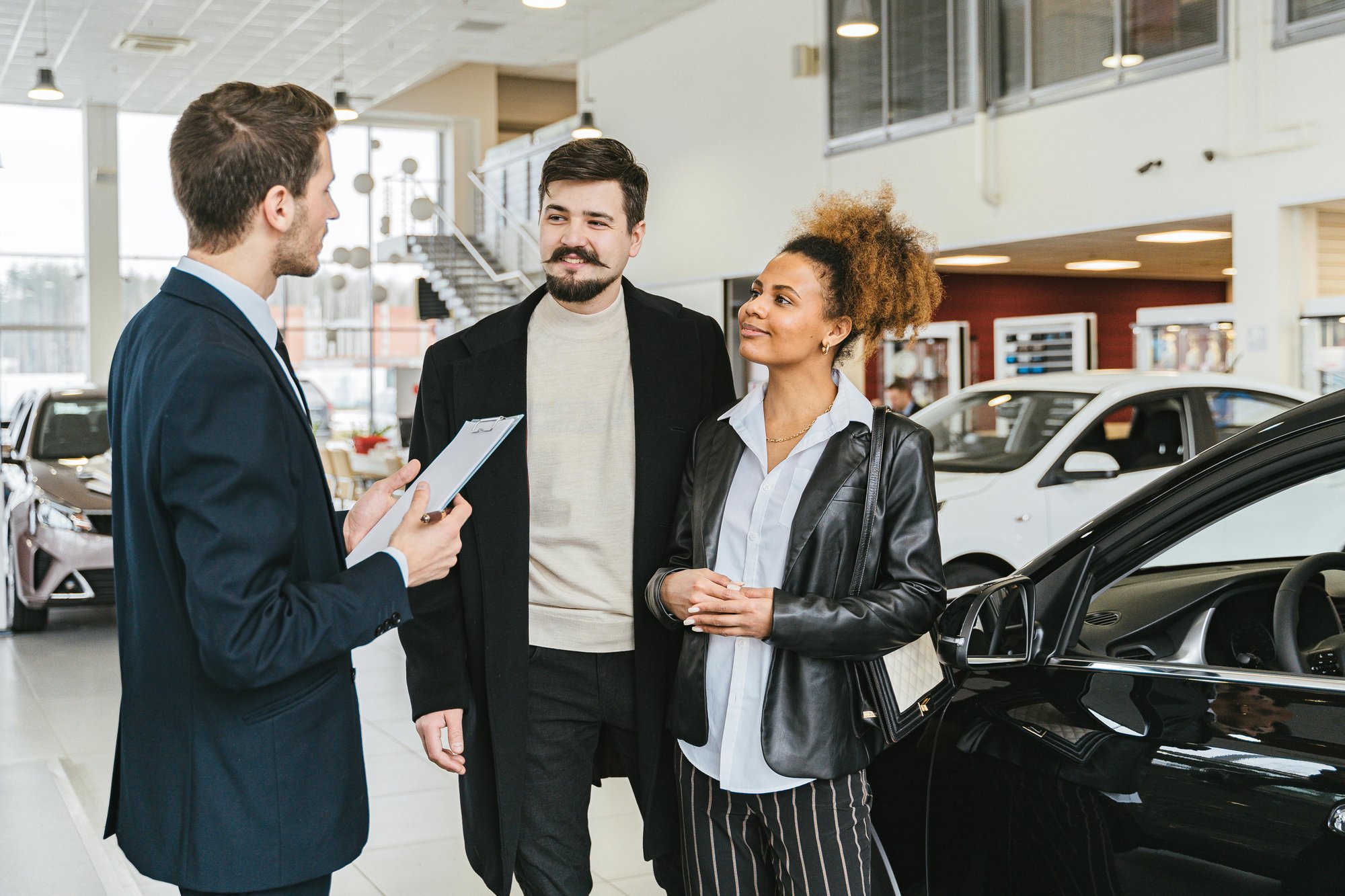 Car sales man talking to couple in front of car